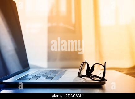 open laptop on which lie reading glasses in black frames. Stock Photo