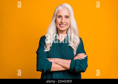 Photo of pretty cheerful white haired grandma lady holding hands crossed responsible chief company ceo founder wear green shirt isolated bright yellow Stock Photo