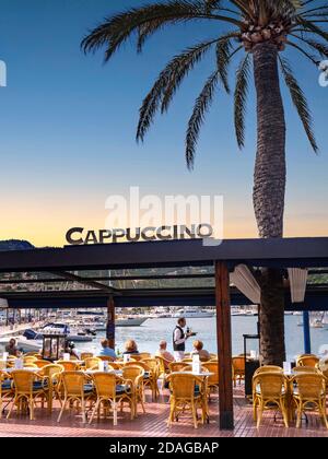 PORT ANDRATX Mallorca alfresco Café Restaurant Cappuccino at sunset dusk, traditional waiter serving refreshments at luxury waterside view marina tables, with feature typical palm tree in Puerto Andratx MALLORCA Spain Balearic Islands Stock Photo