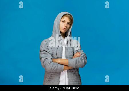 Handsome happy smiling young man wearing gray blouse with crossed arms studio portrait against blue wall Stock Photo