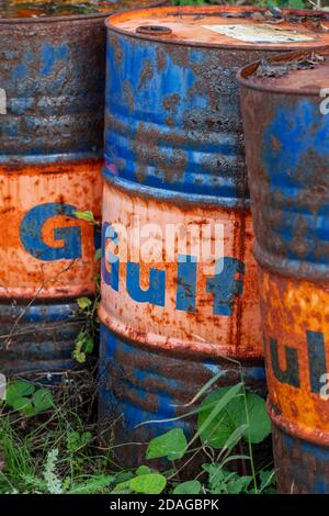 three old colourful oil or chemical metal oil drums rusting way after being discarded. Stock Photo