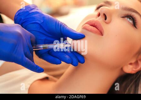 Beautiful woman gets an injection in her face. she has fashion make up and red shining lips Stock Photo