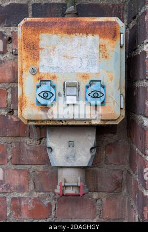 Rusty outdoor electrical outlet with eyes on red brick wall Stock Photo