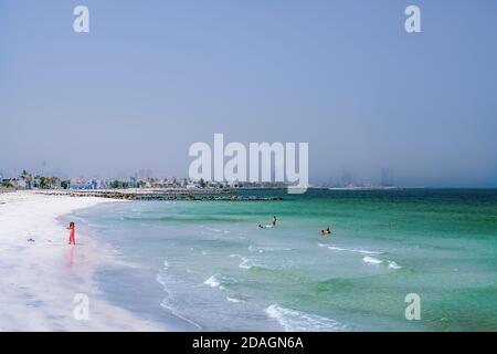 Vacation holidays beach background. Dubai. The Persian Gulf with the line of the beach from the Ajman. Woman in red plays on the beach. Stock Photo