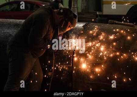 Professional mask protected welder man working on metal welding and sparks of metal at night. Employee welding steel with sparks