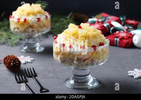 Festive salad with chicken, pineapple, cheese and eggs in portioned bowls on dark gray background. New Year still life. Horizontal format Stock Photo