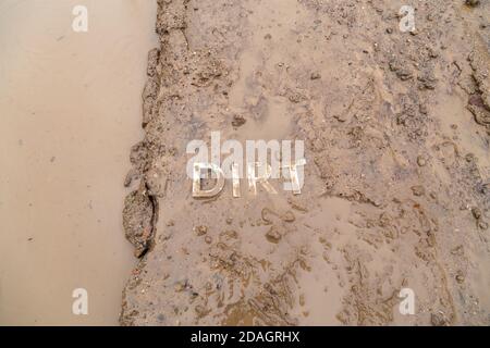 the word mud imprinted in wet dirt road surface and puddle - close-up with selective focus in flat lay perspective. Stock Photo