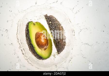 Two halves of avocado splashing into water, isolated on white background. Copy space. Stock Photo