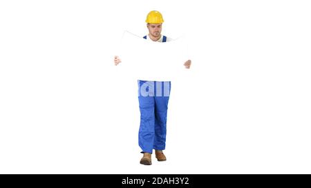 Thoughtful builder in helmet looking at blueprint and walking on white background. Stock Photo