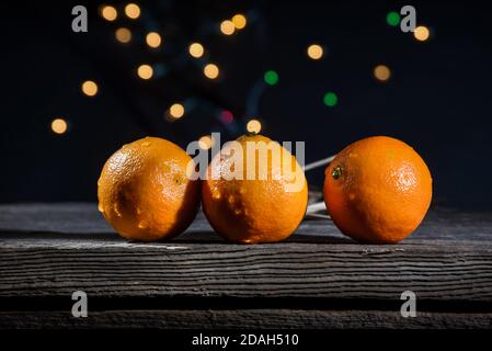 A row of three oranges clementines on a barn wood board with background lights on a black background Stock Photo