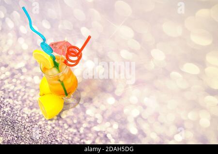 A tall glass of lemon juice with ice and a slice of fruit on the side, decorated with straws and an umbrella, stands on a gray shiny background. Close Stock Photo