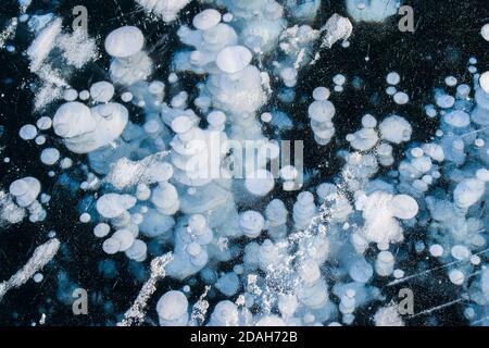 Beautiful transparent blue ice with frozen white methane bubbles. Winter structure of frozen Lake Baikal. Top view. Natural background. copy space. Stock Photo
