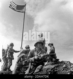 A small flag carried by the 2nd Battalion, 28th Marines is planted atop Mount Suribachi at 10:20 a.m. February 23, 1945. Official NAVY Photo. This is the first flag raising on the top of Mt. Suribachi. The famous flag-raising photo was taken when the second flag was put up later that day. This photo was taken by Leatherneck's Lou Lowery. Stock Photo