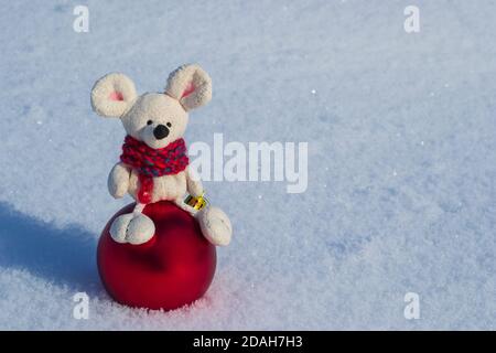 Christmas toy mouse, symbol of the year. In a red knitted scarf with a Christmas red ball. Against the background of white snow Stock Photo