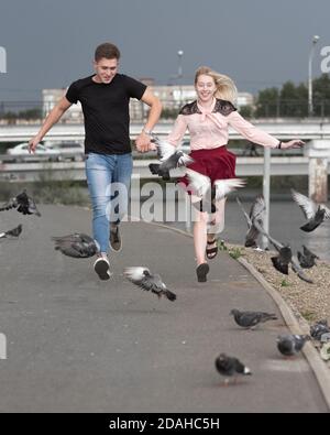 Couple in love holding hands run with pigeons in the city Stock Photo