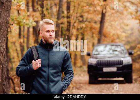 Man traveler on the background of a car in the autumn forest Stock Photo