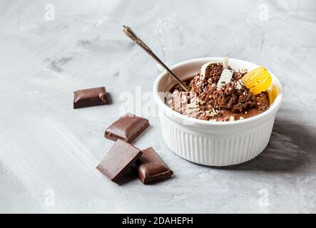 Chocolate mousse garnished with a tangerine wedge and white chocolate shavings in white bowl and pieces of chocolate on a gray table Stock Photo