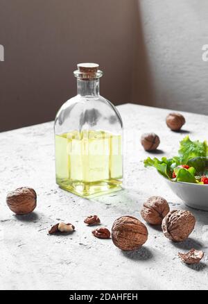 A transparent bottle with cork of walnut oil, walnuts and salad on a gray background, olive oil alternative with unique flavor Stock Photo