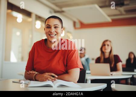 Portrait of a girl sitting in university classroom and smiling. Female student in lecture hall looking at camera and smiling.