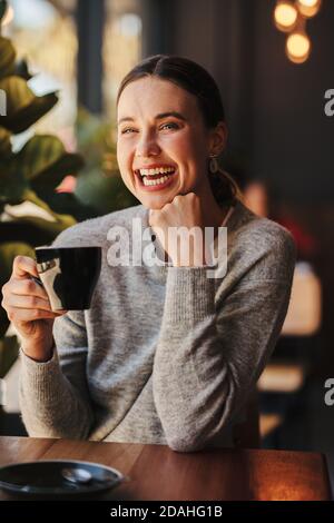 Attractive woman drinking coffee at cafe. Female having a cup of coffee and laughing at coffee shop. Stock Photo