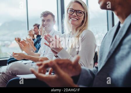 Group of businesspeople sitting at seminar clapping hands. Businessmen and businesswomen applauding after a successful presentation at a conference. Stock Photo