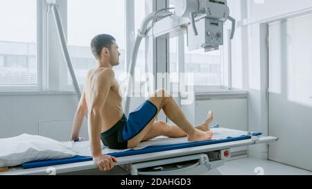 In the Hospital, Man Sitting on a Bed Waiting for X-Ray Machine to Scan His Leg for Injury. Scanning for Fractures, Broken Limbs, Cancer or Tumor Stock Photo