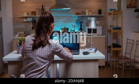 Woman scrolling programming security hacking code data late at night on laptop. Programmer writing a dangerous malware for cyber attacks using performance device during midnight. Stock Photo