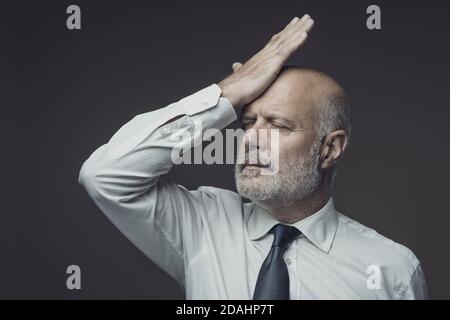 Disappointed businessman touching his forehead, he has made a mistake and feels regretful Stock Photo