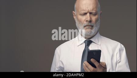 Middle-aged man having difficulties and vision problems using his smartphone, he is unable to read small texts on the screen Stock Photo