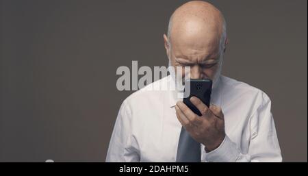 Middle-aged man having difficulties and vision problems using his smartphone, he is unable to read small texts on the screen Stock Photo