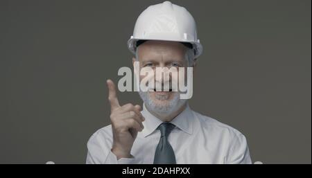 Cheerful businessman and engineer wearing a safety helmet and pointing upwards Stock Photo