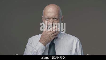 Lazy tired middle-aged businessman yawning and feeling sleepy, he is covering his mouth with his hand Stock Photo