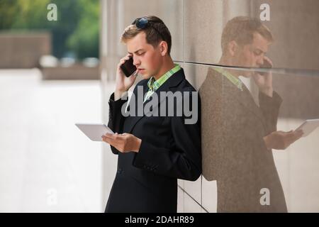Young business man in black blazer using digital tablet computer and calling on cell phone Stock Photo