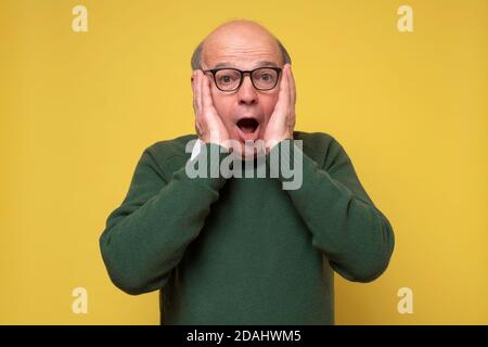 Surprised caucasian man with glasses holding hands near face. Stock Photo