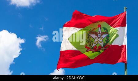 Low angle shot of the flag of Santa Catarina on a flagpole under a blue sky and sunlight in Brazil Stock Photo