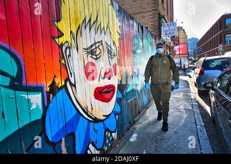 GREAT BRITAIN / England / London / A man with face mask walks past graffiti depicting Prime minister Boris Johnson as a clown, near Brick Lane . Stock Photo