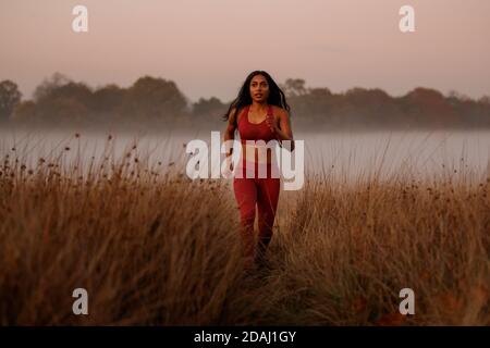 A woman of Asian descent running in a misty park at sunset Stock Photo
