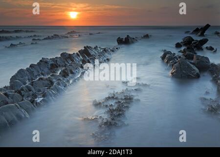 View of the rock ledges at sunset at Welcombe Mouth Beach on the Devon and Cornwall border Stock Photo