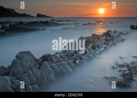 View of the rock ledges at sunset at Welcombe Mouth Beach on the Devon and Cornwall border Stock Photo