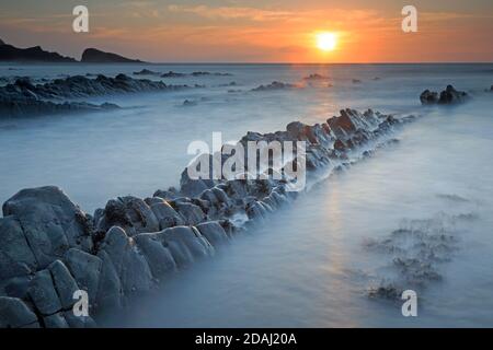 View of the rock ledges at sunset at Welcombe Mouth Beach on the Devon and Cornwall border Stock Photo