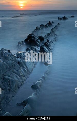 View of the rock ledges at sunset at Welcombe Mouth Beach on the Devon and Cornwall border Stock Photo