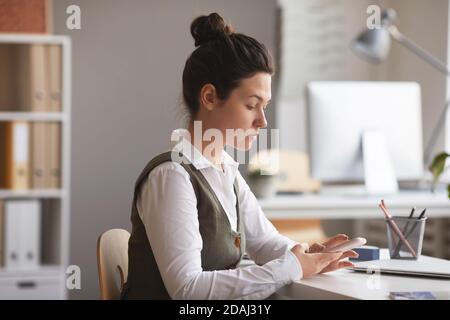 Serious young businesswoman concentrating on her online work on mobile phone sitting at office Stock Photo