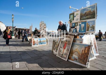 Artists sell their paintings to tourists on the central promenade of the Riva degli Schiavoni (Slavyanskaya) on a sunny day in Venice, Italy.