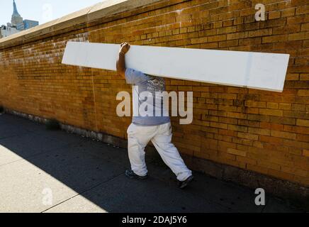New York, USA - Sep 23, 2017: Manhattan street scene. Cargo delivery. A worker carries in his hands large white boards along the brick fence on the st Stock Photo