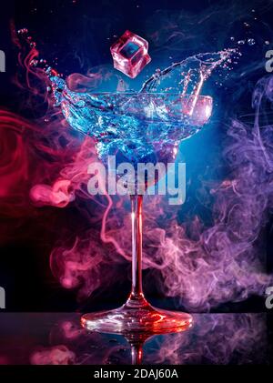 ice cube falling into splashing cocktail on smoky background Stock Photo