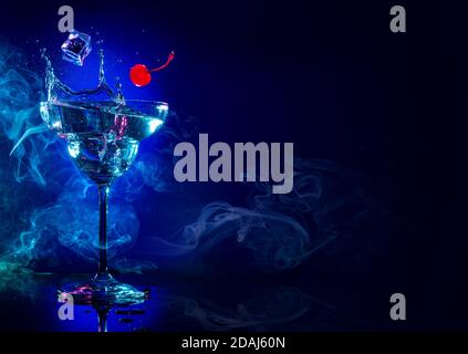 ice and cherry falling in a cocktail splash on blue smoky background Stock Photo