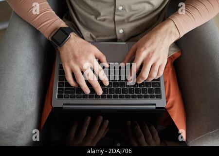 Close-up of man sitting on armchair and typing on laptop computer Stock Photo