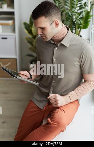 Young man holding digital tablet in his hands and watching something while sitting in the room Stock Photo