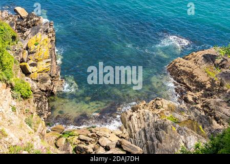 Waves crashing on rocks on the bank of Fowey Estuary, Fowey, Cornwall, UK Stock Photo