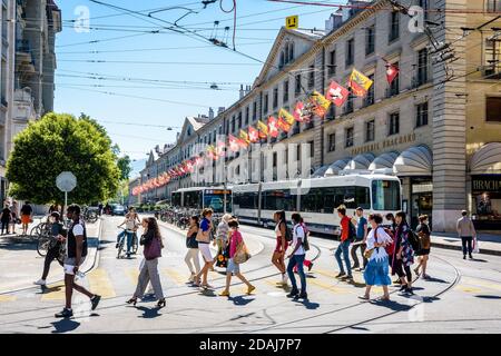 Pedestrians are crossing the rue de la Corraterie in Geneva, with buildings decked with flags, as a bus and a streetcar are passing each other. Stock Photo